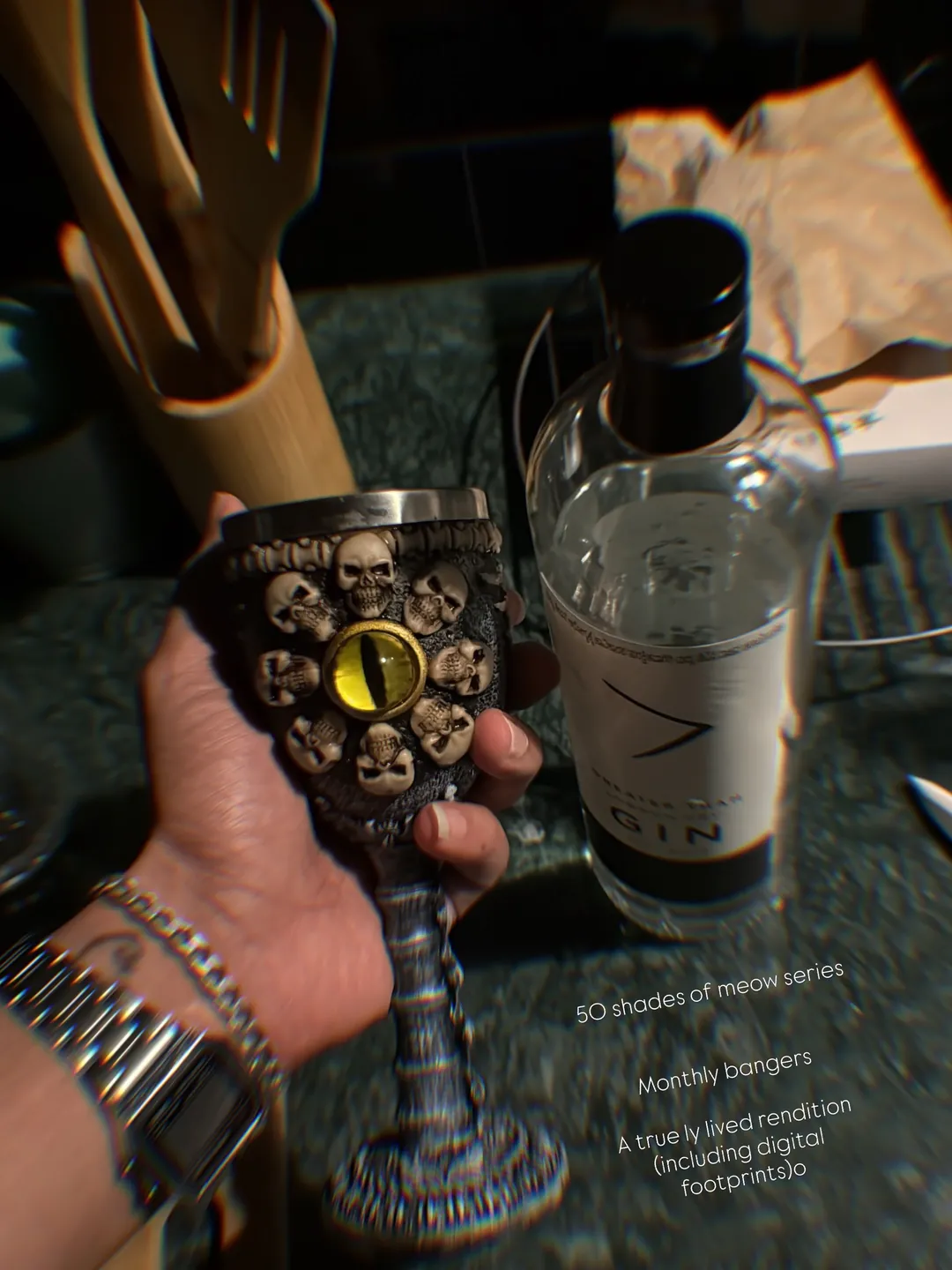 A hand holds a skull-studded goblet beside a gin bottle, with the series card: 50 shades of meow series, monthly bangers, a truly lived rendition including digital footprints