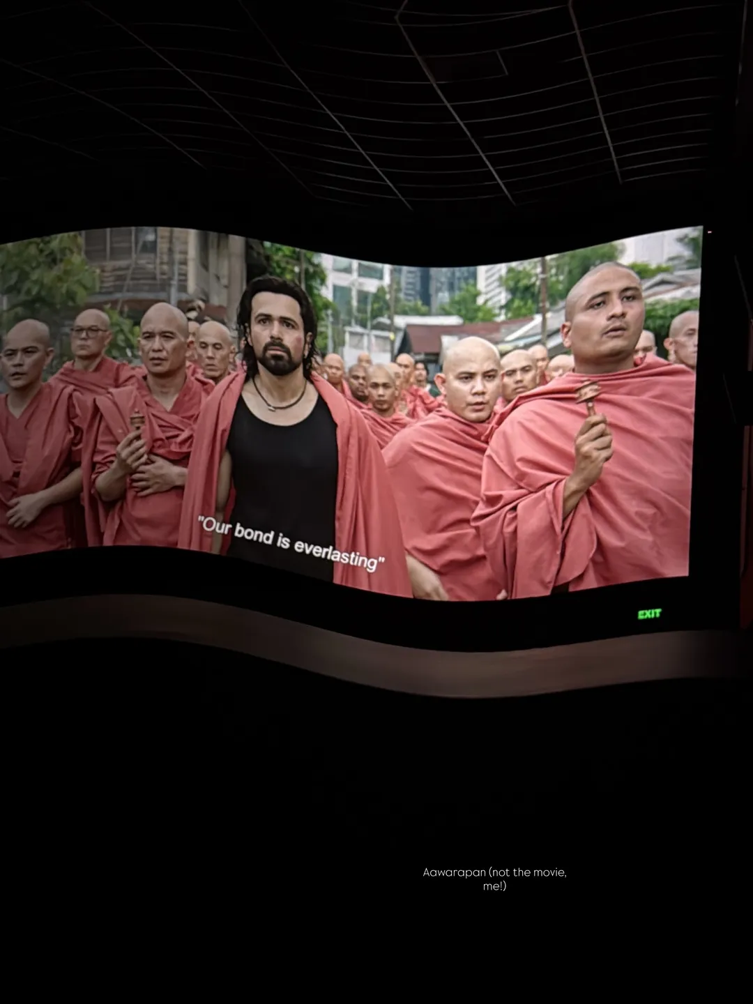 A cinema screen showing monks in a film scene, subtitled: our bond is everlasting
